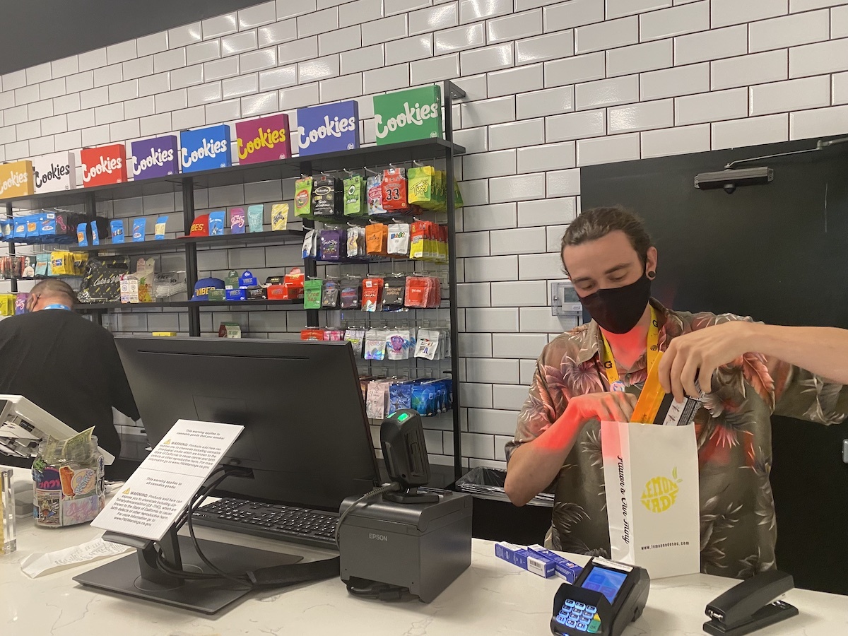 A budtender checks out cannabis customers, with a wall of products behind them